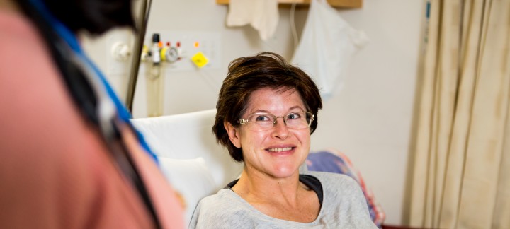 A close up of a female patient sitting up in bed, smiling.
