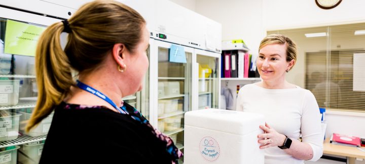 A woman holds a styrofoam box while smiling at another woman in a lab room
