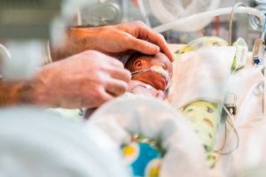 Medium close up of a small, premature baby connected to tubes and lying in a neonatal bed.