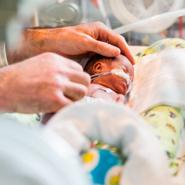 Medium close up of a small, premature baby connected to tubes and lying in a neonatal bed.