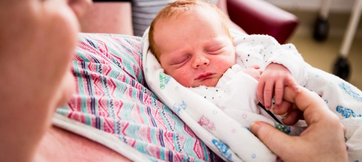 A close up of a new born baby being held while sleeping.